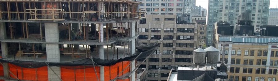 An active high-rise construction site in Manhattan, with workers on an open concrete floor deck, rebar and formwork, and safety netting strung between floors