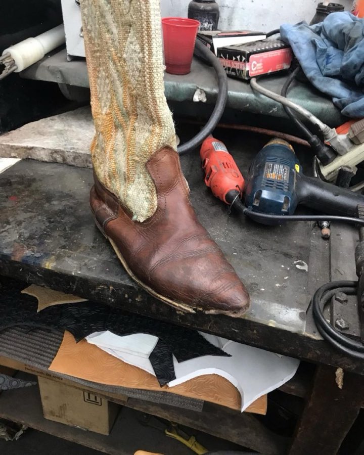 A brown leather boot being reheeled on the workbench with power tools nearby