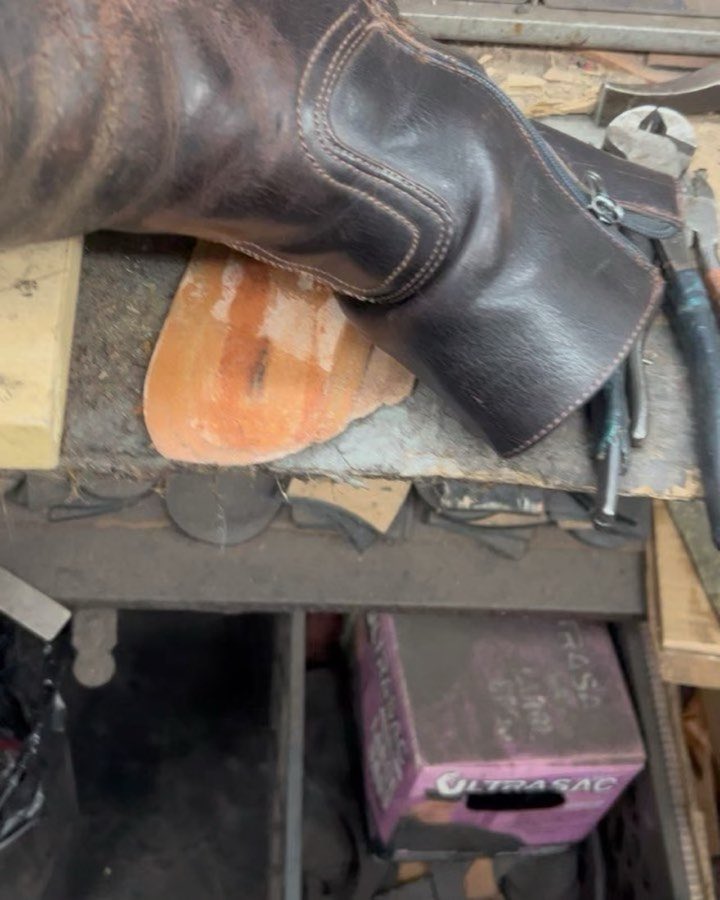 A boot sole mid-repair on the workbench, surrounded by tools and patch material
