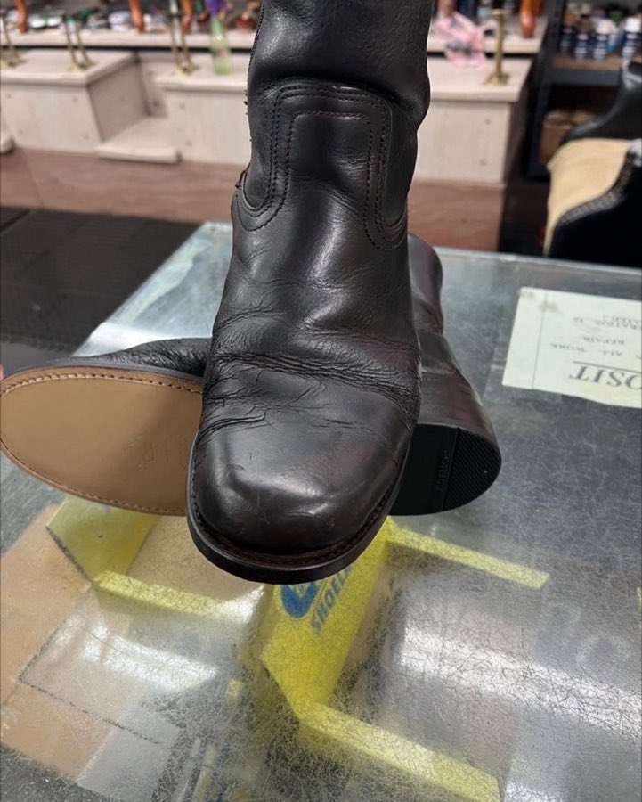 Close-up of a repaired dark brown leather boot standing on the shop's glass counter