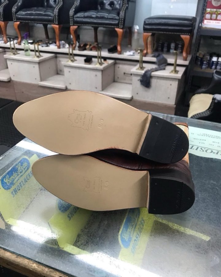 A pair of men's dress shoes, freshly resoled, soles-up on the glass counter
