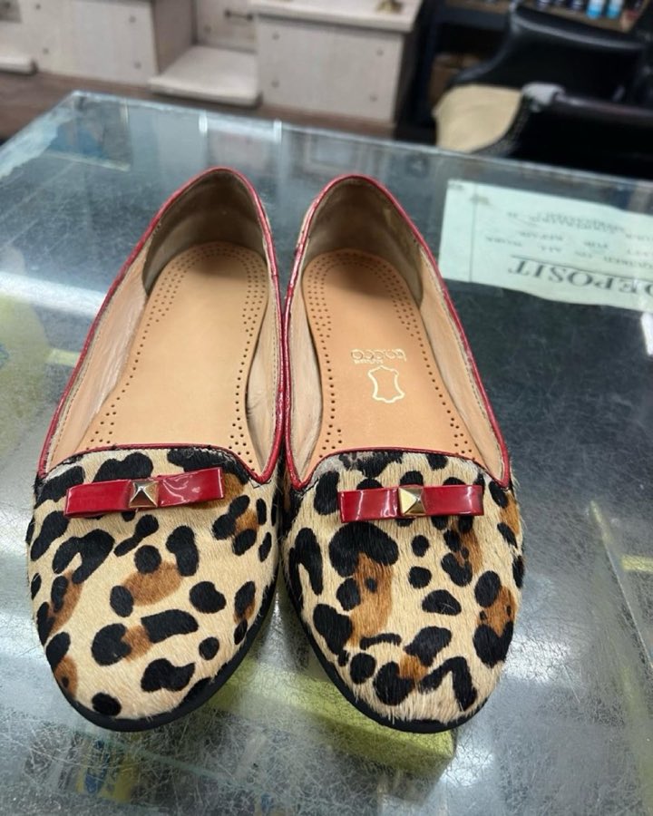 Leopard-print calf-hair flats with a red bow trim, on the shop's glass counter