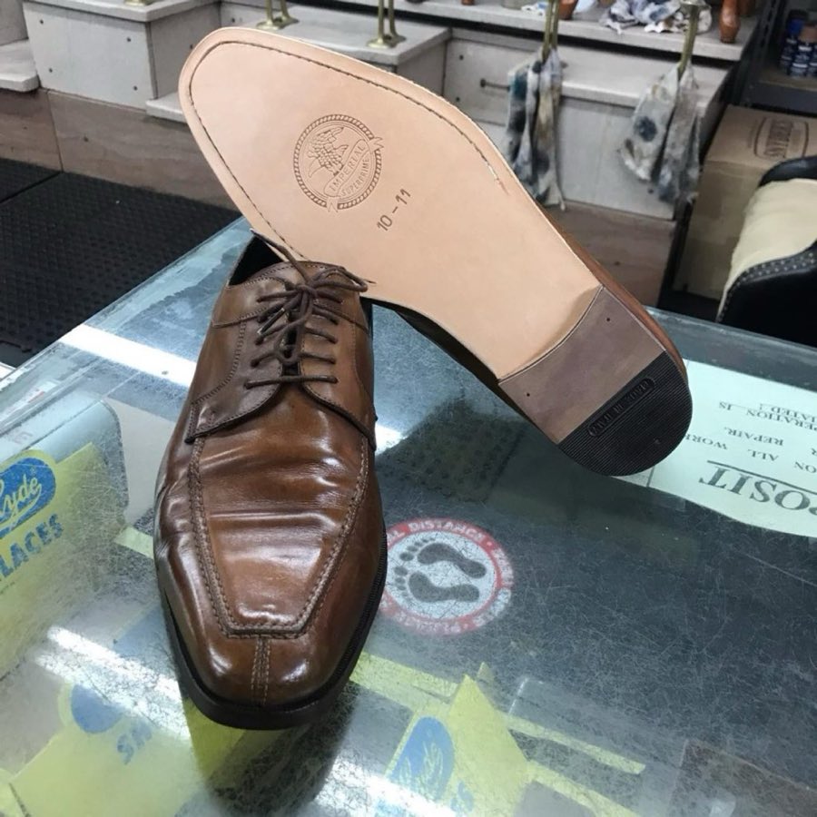 Black leather cap-toe oxfords, freshly resoled, soles-up on the counter