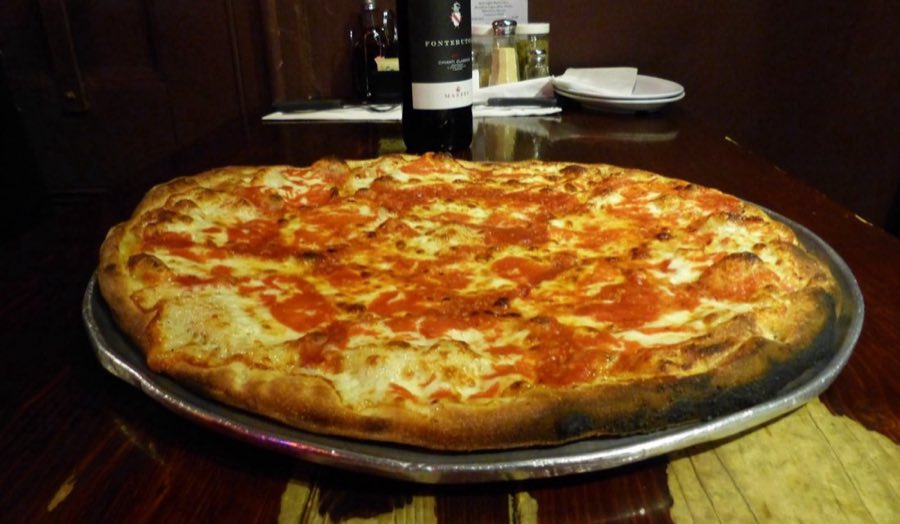 A whole pizza on a metal tray on a checkered tablecloth in the dim dining room