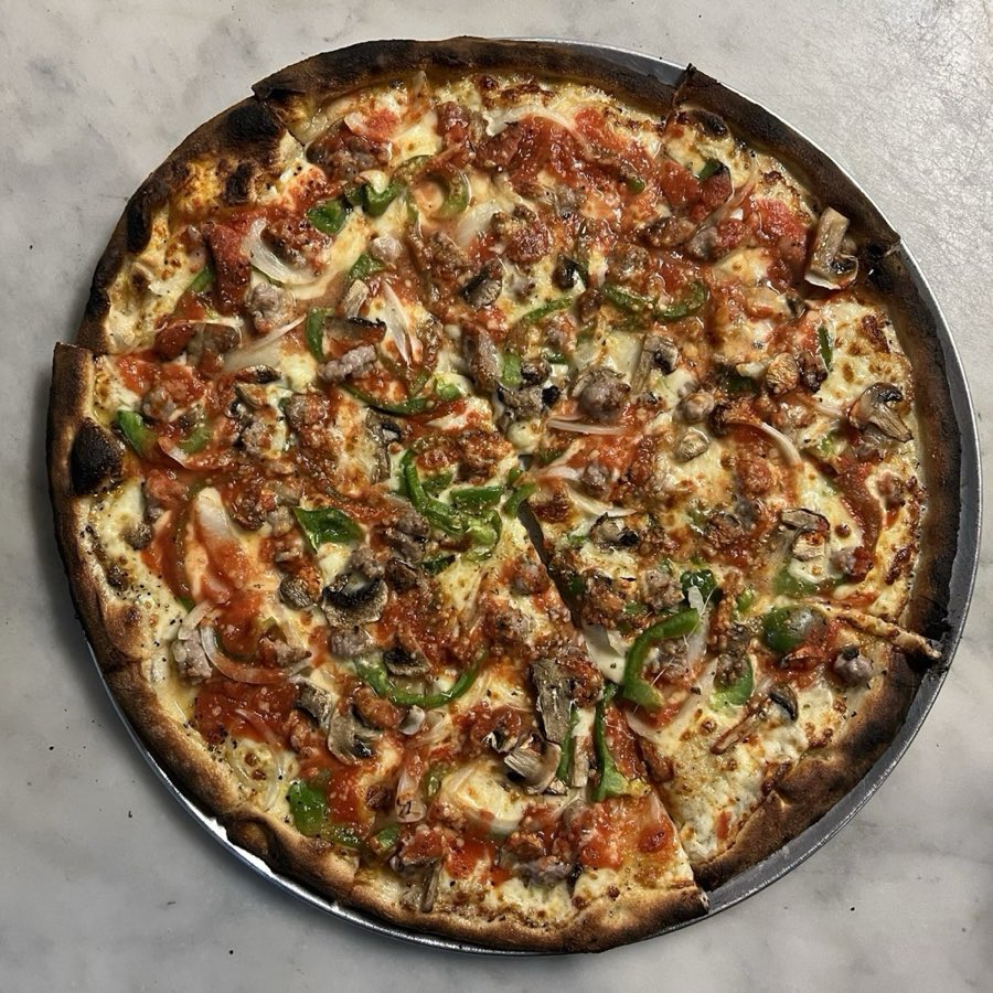 Overhead view of a char-blistered coal-oven pizza topped with sausage, mushroom, green pepper and onion, fresh from the oven