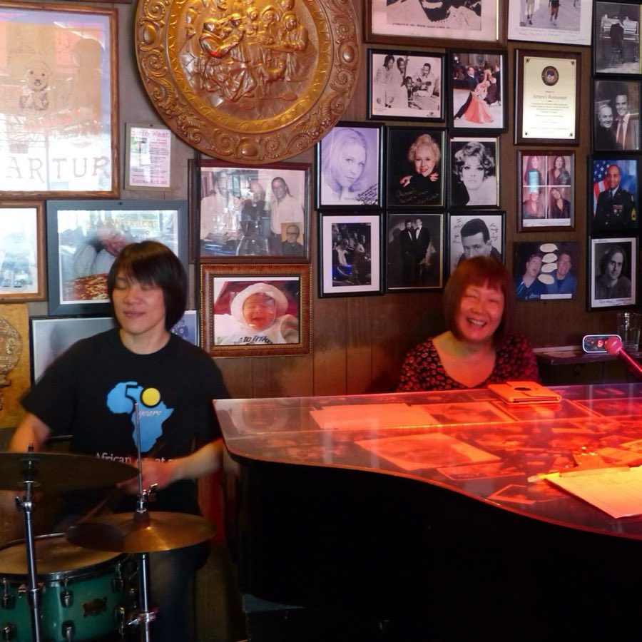 A pianist performing against a wall covered in black-and-white photographs and memorabilia