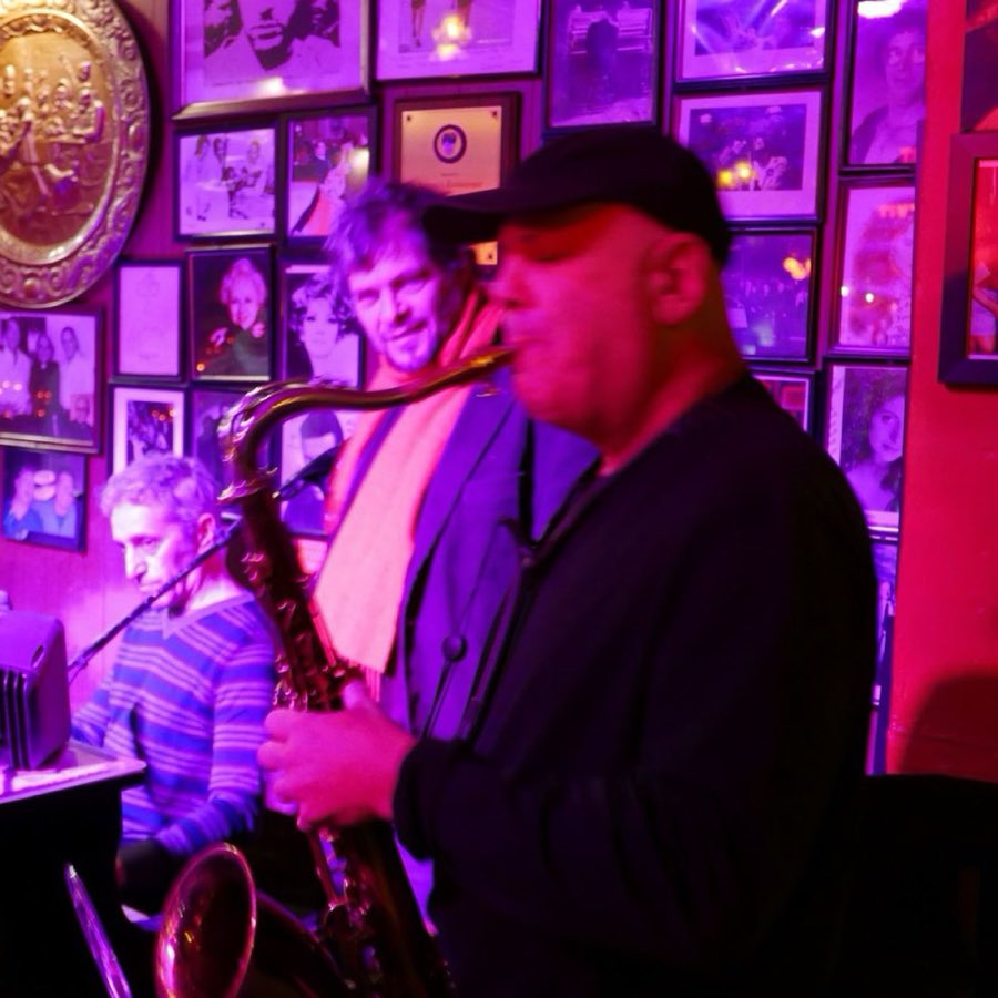 A saxophone and guitar duo performing together under red light