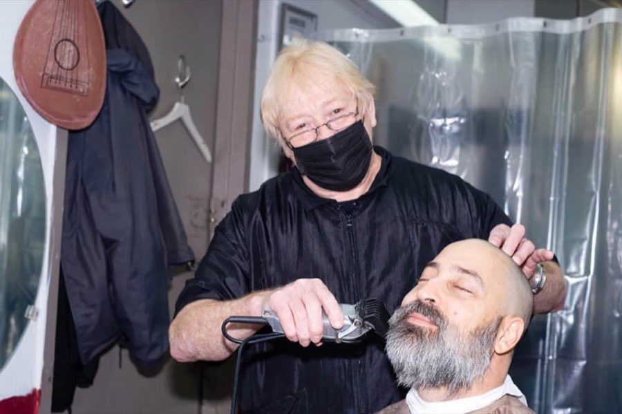 Documentary-style photograph of a barber shaving a bald customer's head with a straight razor during the pandemic