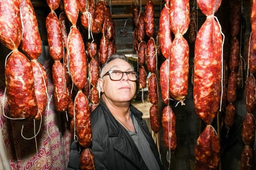 A barber standing among rows of hanging cured salami in a curing room