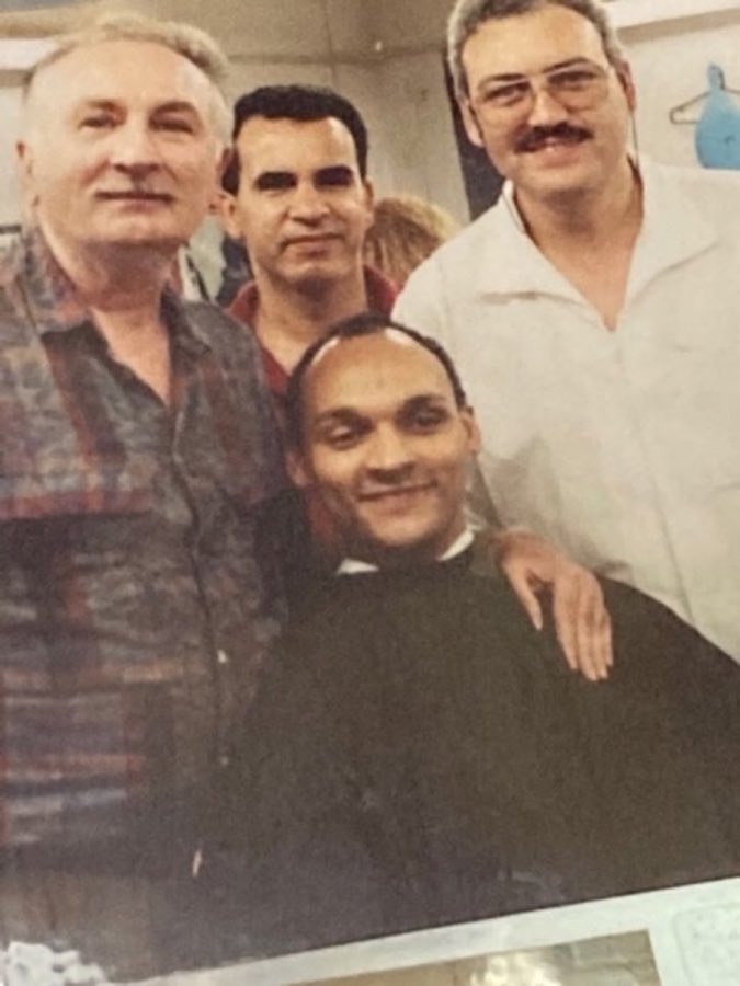 A vintage group photo from the shop wall showing four men, one in a barber smock