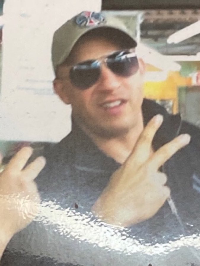 Photo from the shop wall of a customer identified as Vin Diesel with a barber, wearing sunglasses