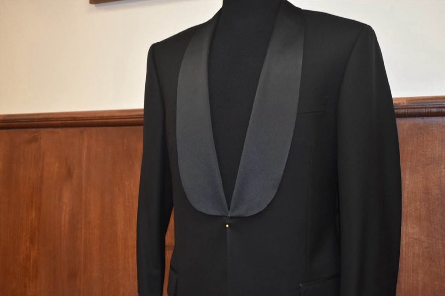 Black shawl-collar tuxedo jacket on a mannequin with the storefront window reflected behind it