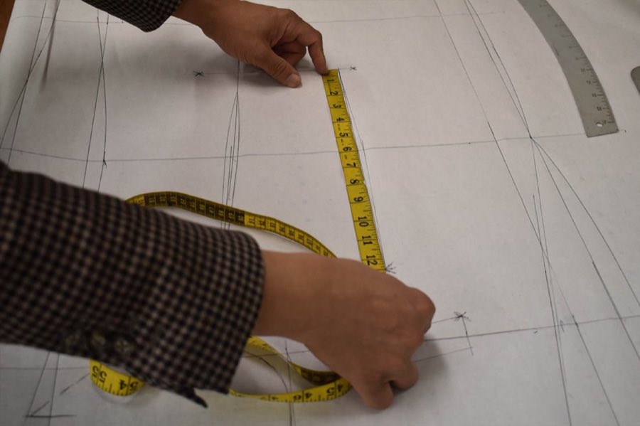 Tailor's hands marking chalk lines on fabric at the cutting table