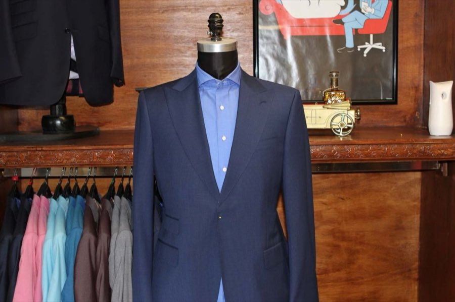 Navy suit and blue shirt on a mannequin with a framed illustration and a rack of suits behind it