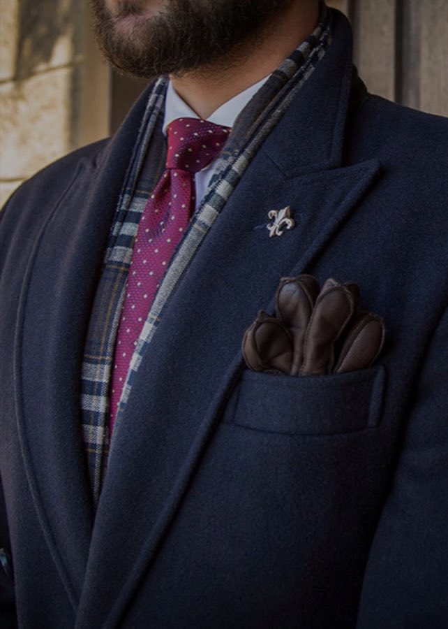 Man in a navy suit and burgundy tie standing outdoors against a stone wall