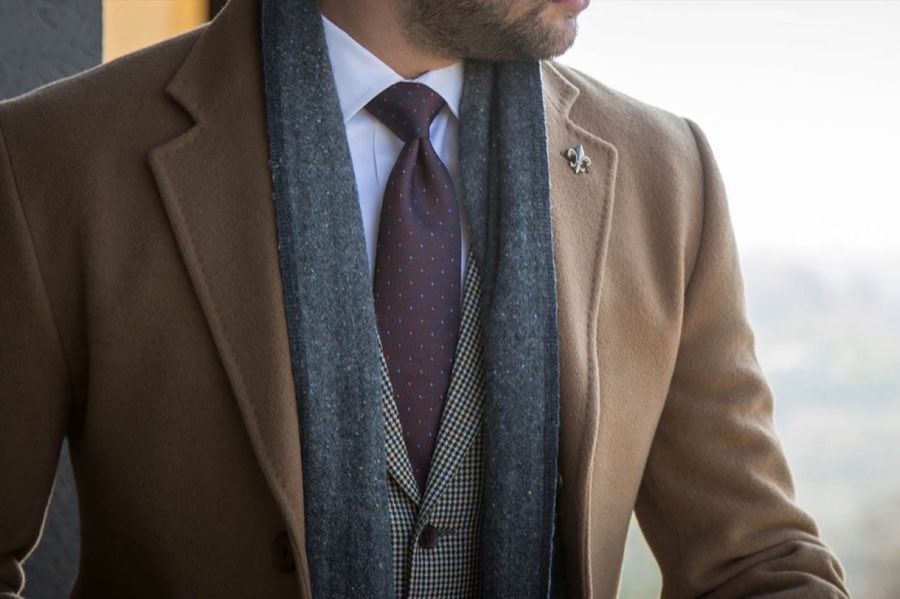 Man wearing a tan suit with a brown tie and pocket square against a warm lit backdrop
