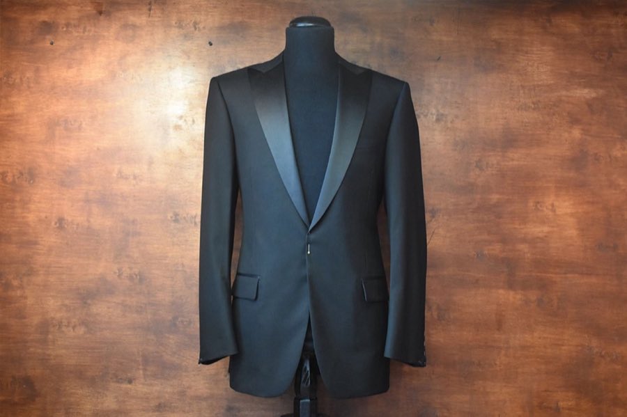Dark teal suit jacket on a mannequin against a warm brown backdrop