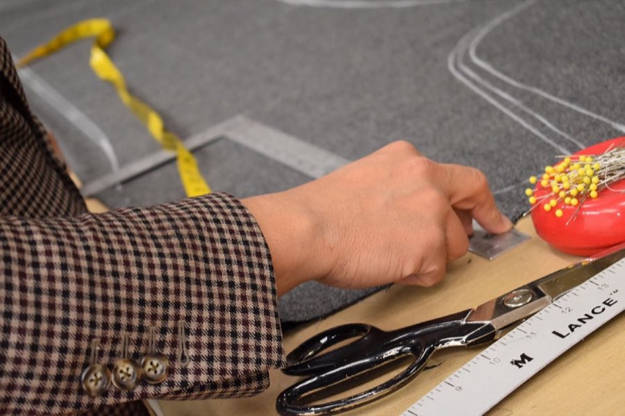 Tailor's hands cutting chalk-marked wool fabric with shears and a tape measure on the cutting table