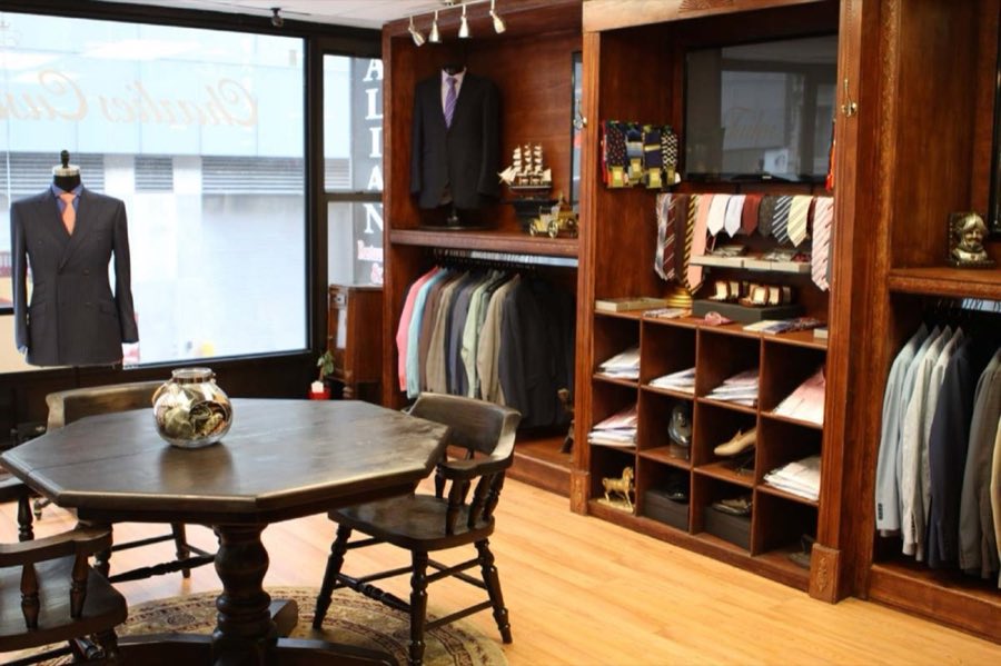 Wide view of the shop interior with racks of finished suits arranged by color and wooden shelving