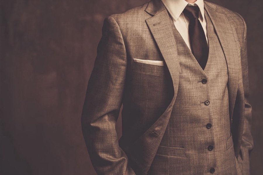 Tan three-piece suit with vest and dark tie in moody, warm lighting