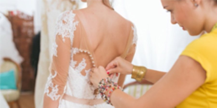 A bride's dress being fitted and buttoned at the back by a staff member