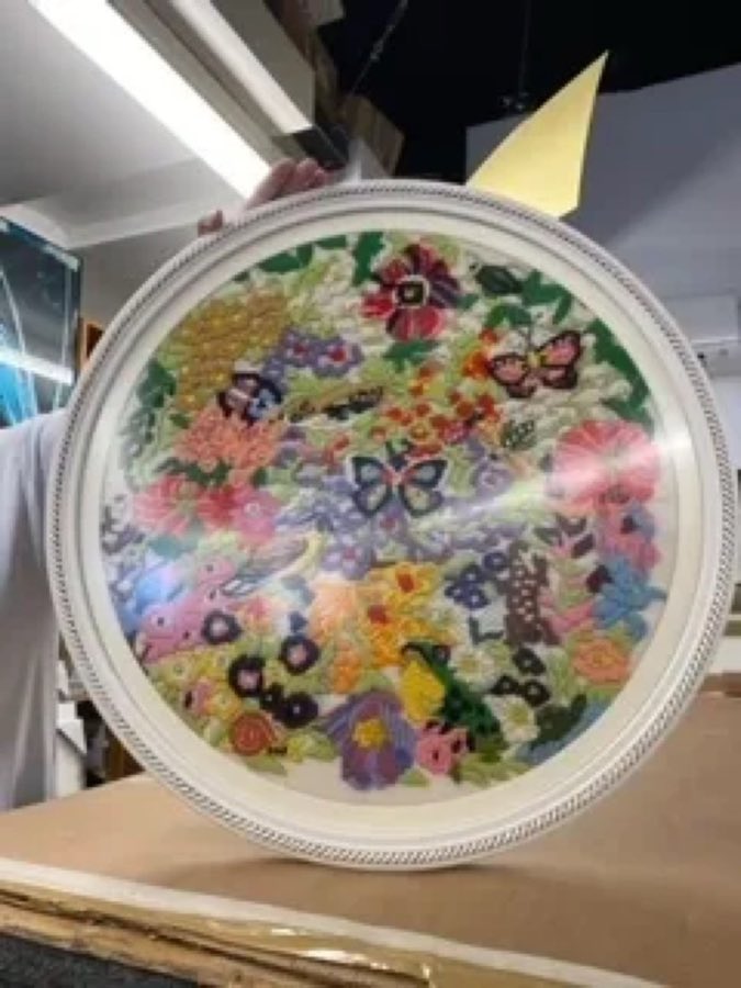 A round embroidered floral needlepoint piece, custom-framed in a white circular frame