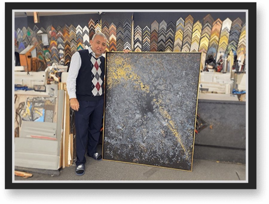 Sediq, the owner of Columbus Art Gallery, standing beside a large framed abstract painting in front of a wall of frame corner samples