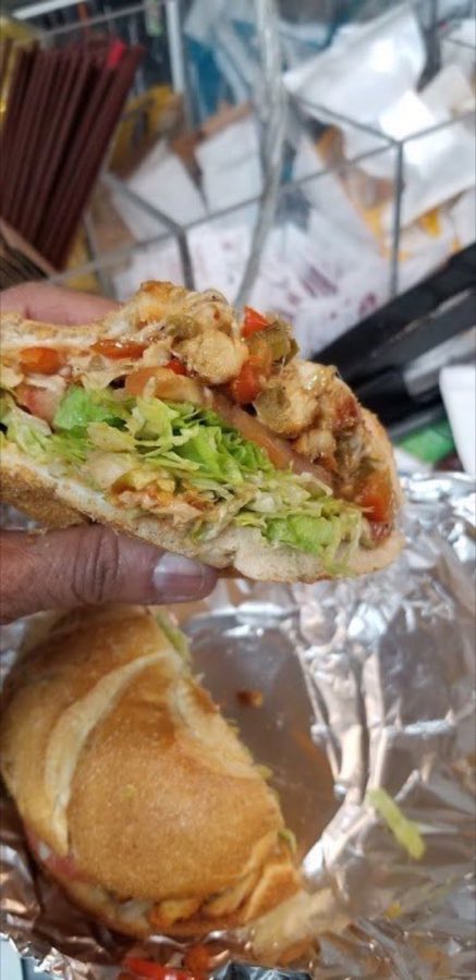 A fresh-cut made-to-order hero sandwich with chicken, lettuce, tomato, and peppers, held open on foil wrap