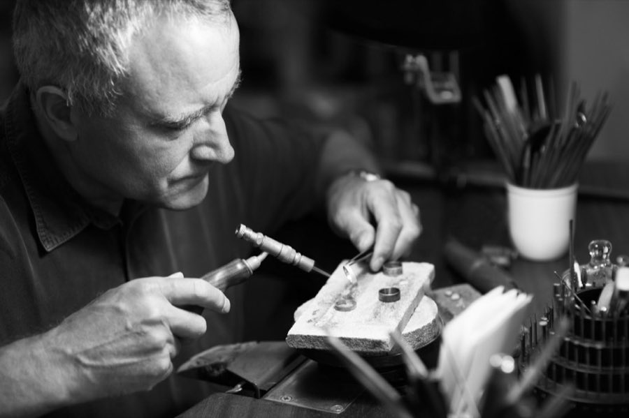 A jeweler at DRS NY Corp. carefully soldering a ring at the workbench, tools blurred in the background