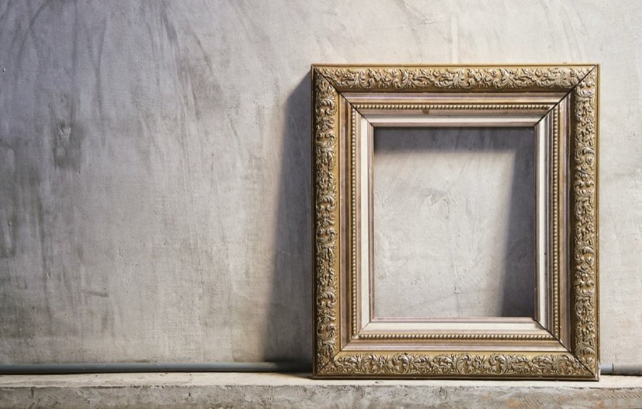 An ornate antique gold picture frame, empty, standing against a raw plaster wall