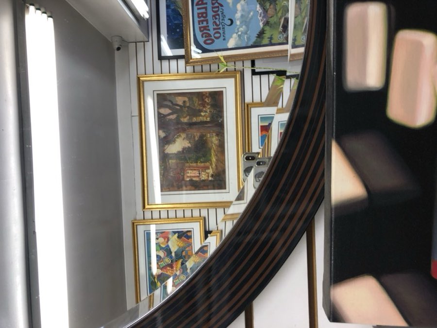 A curved custom mirror reflecting the shop's wall of frame samples