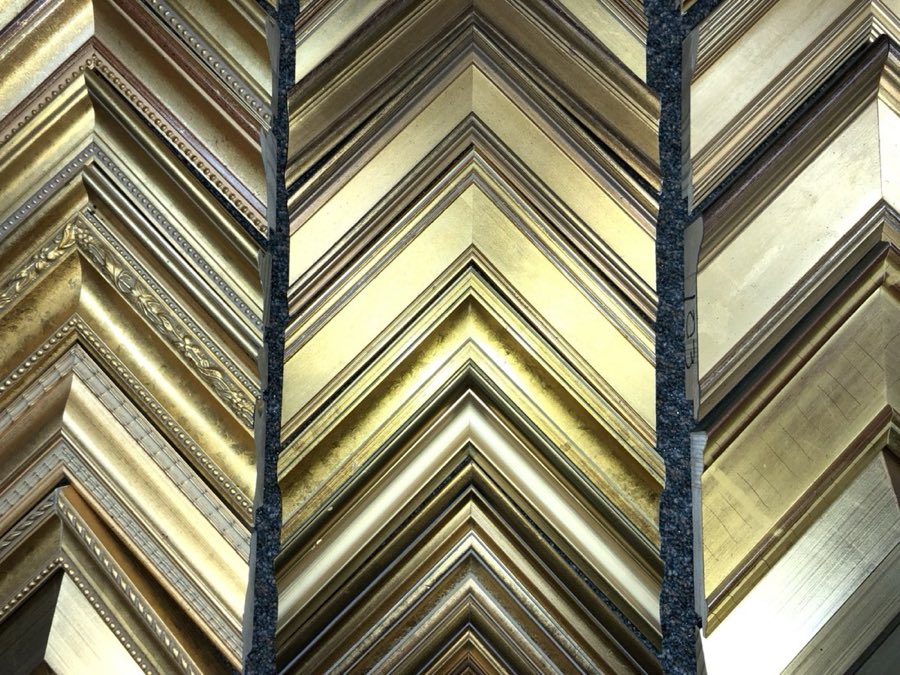 Close-up of ornate gold frame moulding corner samples stacked at the shop