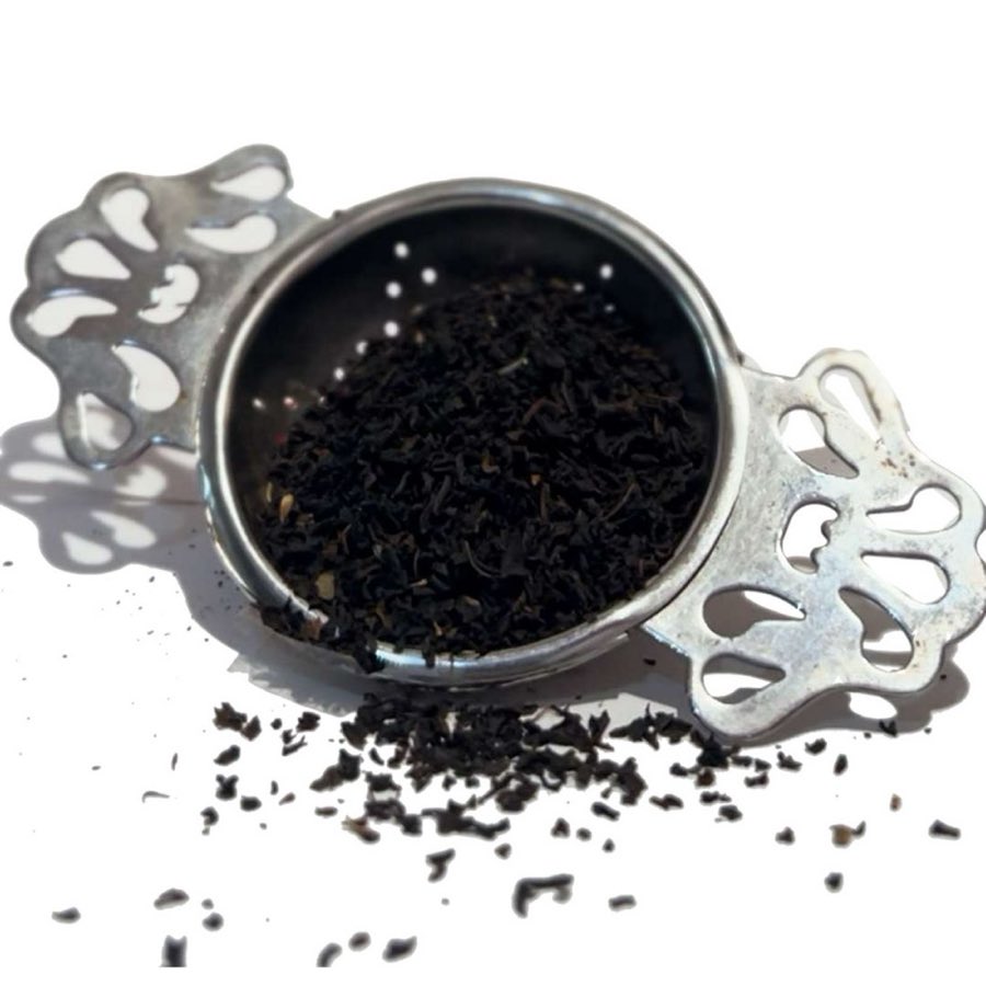 Loose Assam black tea leaves in a small ornate metal tea strainer