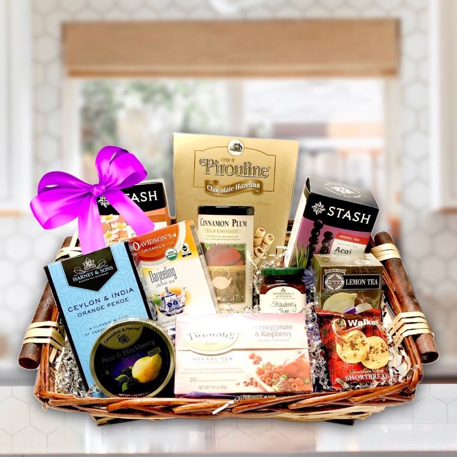 A wicker gift basket filled with boxed teas from Harney & Sons, Stash, Twinings, Davidson's Organics, and Mlesna, along with Pirouline wafers, Stonewall Kitchen jam, and Walkers shortbread