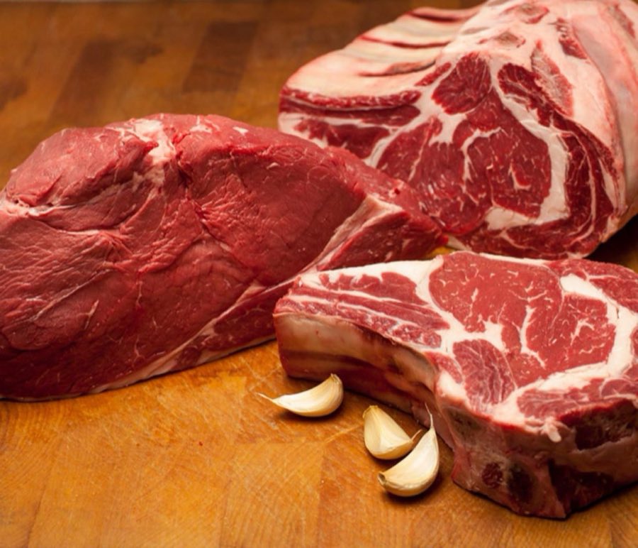 Raw beef roast, rib steaks, and garlic cloves on a wooden butcher block