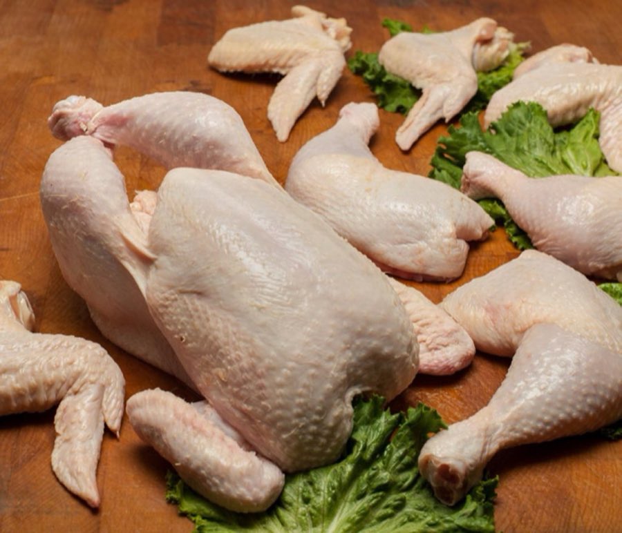 A raw whole chicken and cut chicken pieces on lettuce leaves atop a wooden butcher block