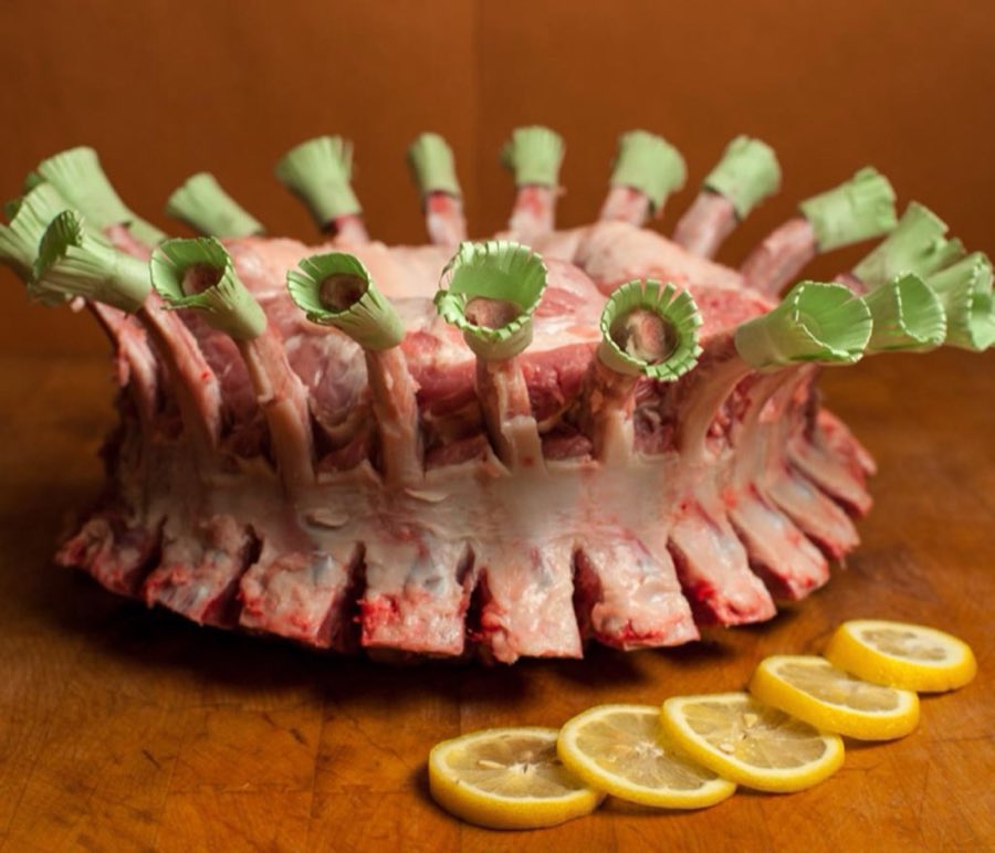 A crown roast of pork with paper frills, styled and plated with lemon slices