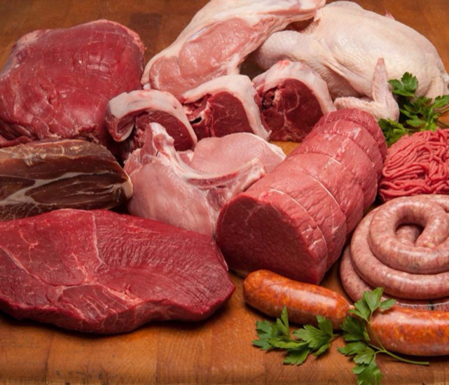A butcher-block table spread with a beef roast, rib steaks, a whole chicken, sausage links, ground beef, and cured ham