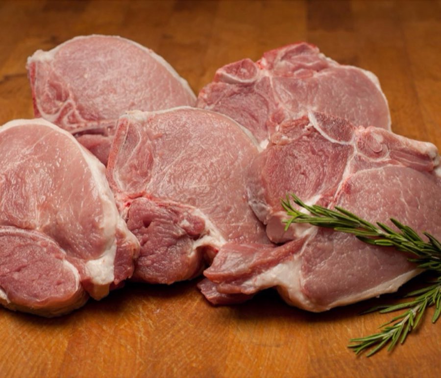 Raw pork chops with a sprig of rosemary on a wooden butcher block
