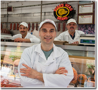 Three staff members in white butcher coats behind the counter, with a Boar's Head Brand neon sign overhead