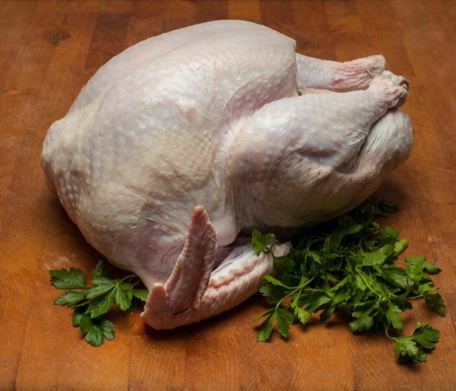 A raw whole turkey with fresh parsley on a wooden butcher block
