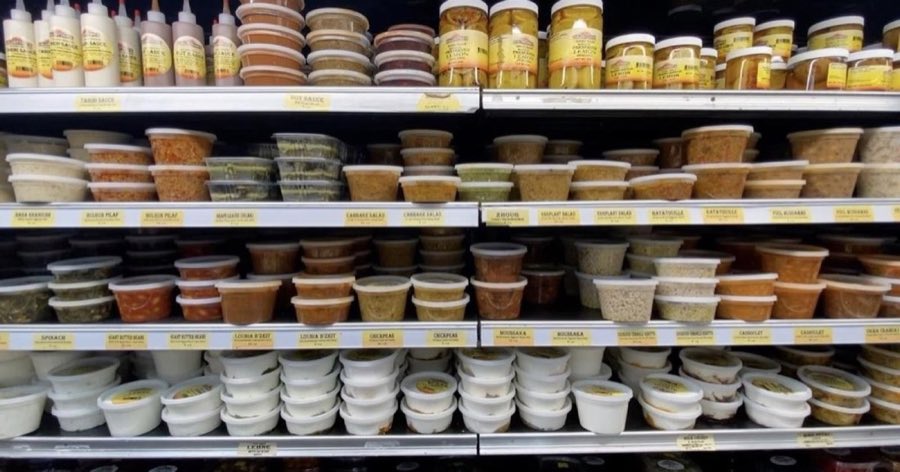 Refrigerated deli case at Kalustyan's stocked with prepared foods in labeled containers: baba ghanoush, bulgur pilaf, grape leaves dolma, cabbage salad, zhoug, eggplant salad, ratatouille, ful medames, moussaka, couscous tabbouleh, cassoulet, okra, spinach, and lebne