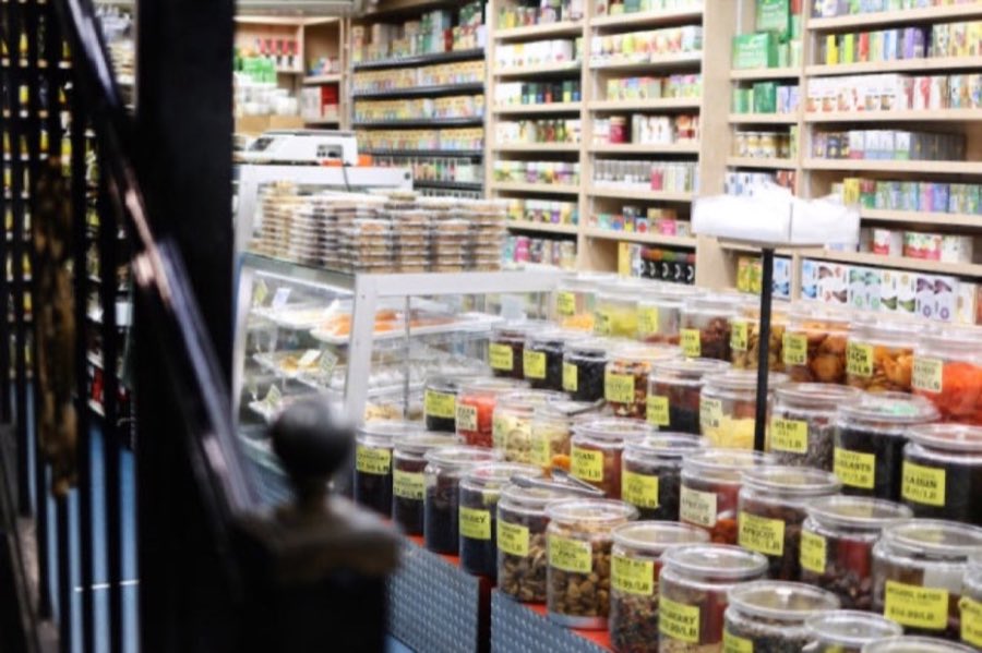 Inside Kalustyan's: shelves packed floor to ceiling with spice tins and boxes, a glass pastry case, and bins of dried fruit and nuts with hand-written yellow price tags