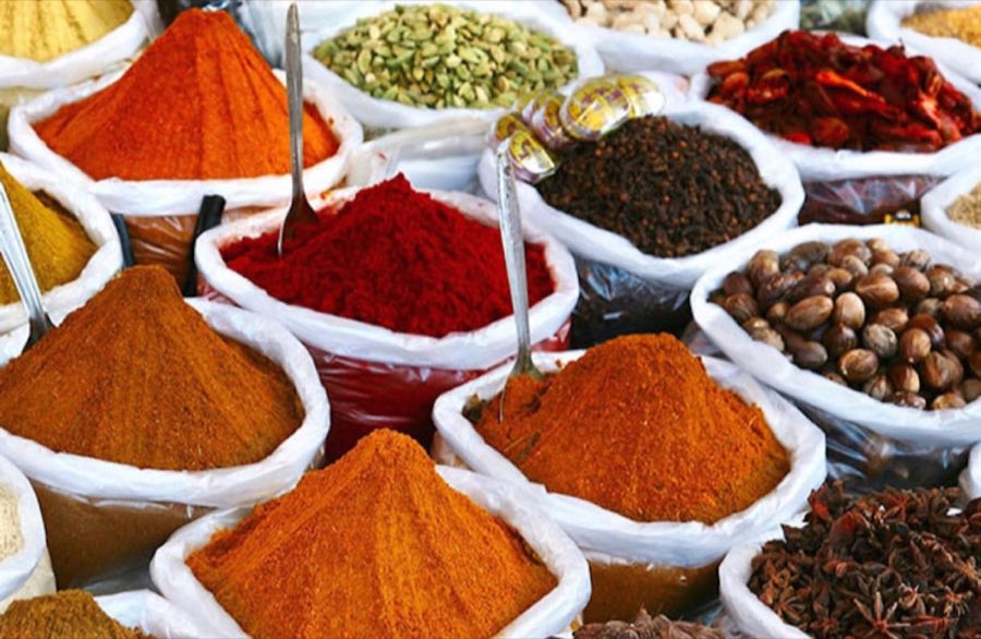 Studio close-up of whole cloves, cinnamon, cumin, cardamom, coriander, black peppercorns, dried chilies, star anise and nutmeg surrounding a bowl of ground spice