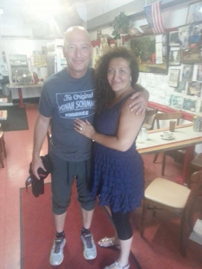 Inside the shop: a visitor poses in a shop T-shirt on the red-and-white checkerboard floor, beside red-topped diner tables and a wall covered edge to edge with framed photographs
