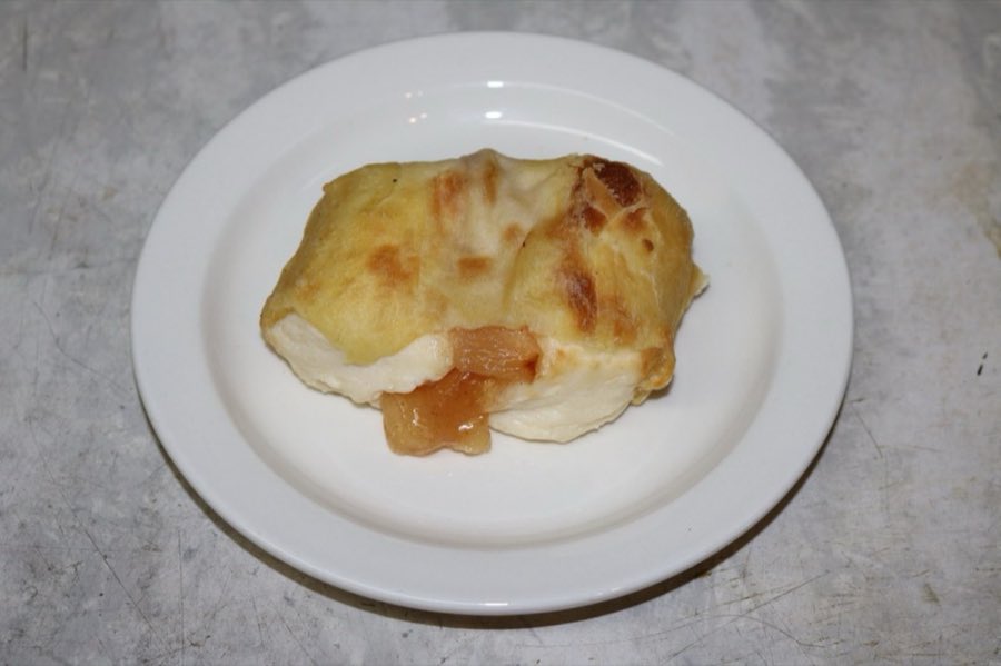 A baked golden sweet knish split open, showing apple filling, on a white plate