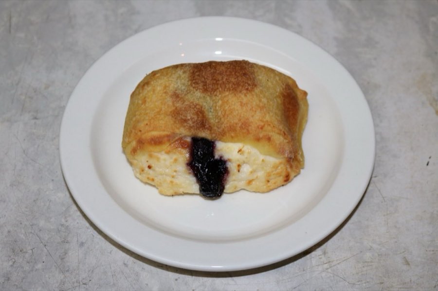 A baked sweet knish with blueberry filling visible, on a white plate