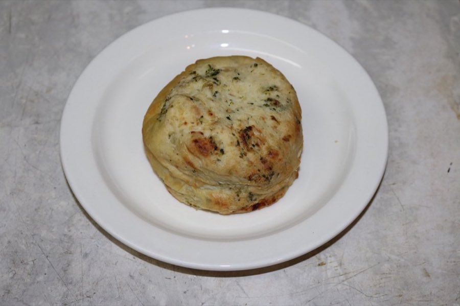 A round baked knish filled with broccoli, on a white plate
