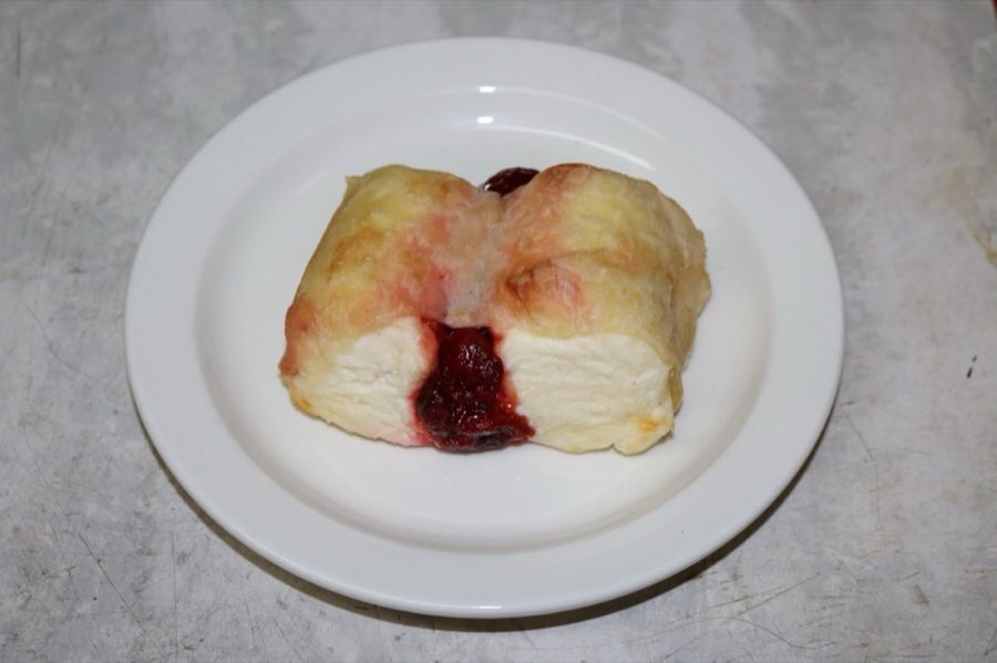A baked sweet knish with cherry filling visible, on a white plate