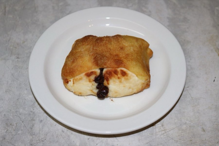 A baked sweet knish with chocolate filling visible, on a white plate